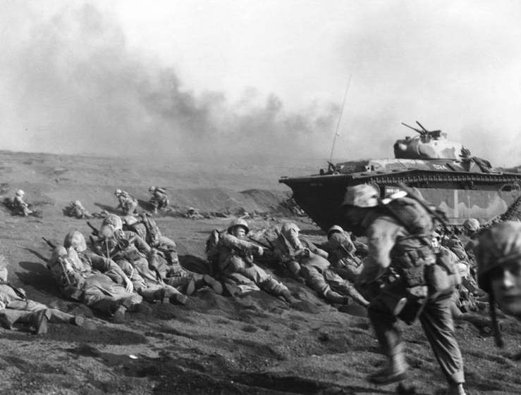 U.S. Marines of the Second Battalion, Seventh Regiment, wait to move inland on Iwo Jima, soon after going ashore on 19 February 1945. An LVT(A)-5 amphibious tractor is in the background. Source: Wikipedia.