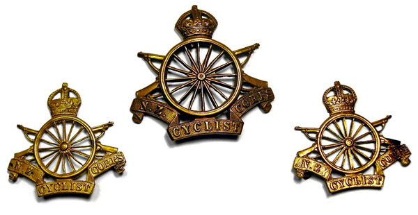 Cap and collar badges: Wheel with crossed rifles surmounted by a crown and a scroll underneath with the words ‘NZ Cyclist Corps’.